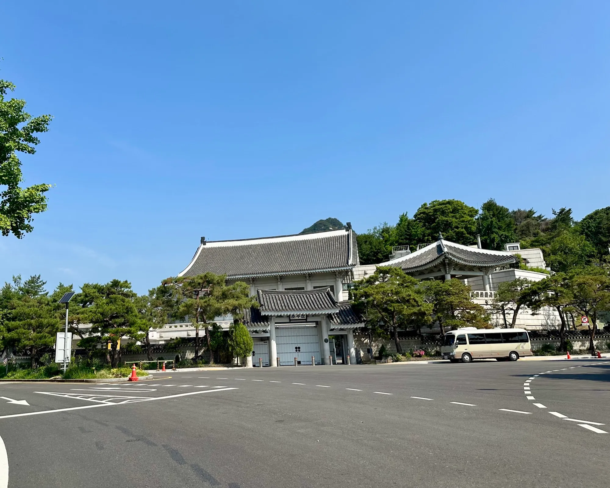 The blue-tiled traditional buildings of the Blue House (Cheong Wa Dae) set against the forested slope of Bugaksan under a clear sky.