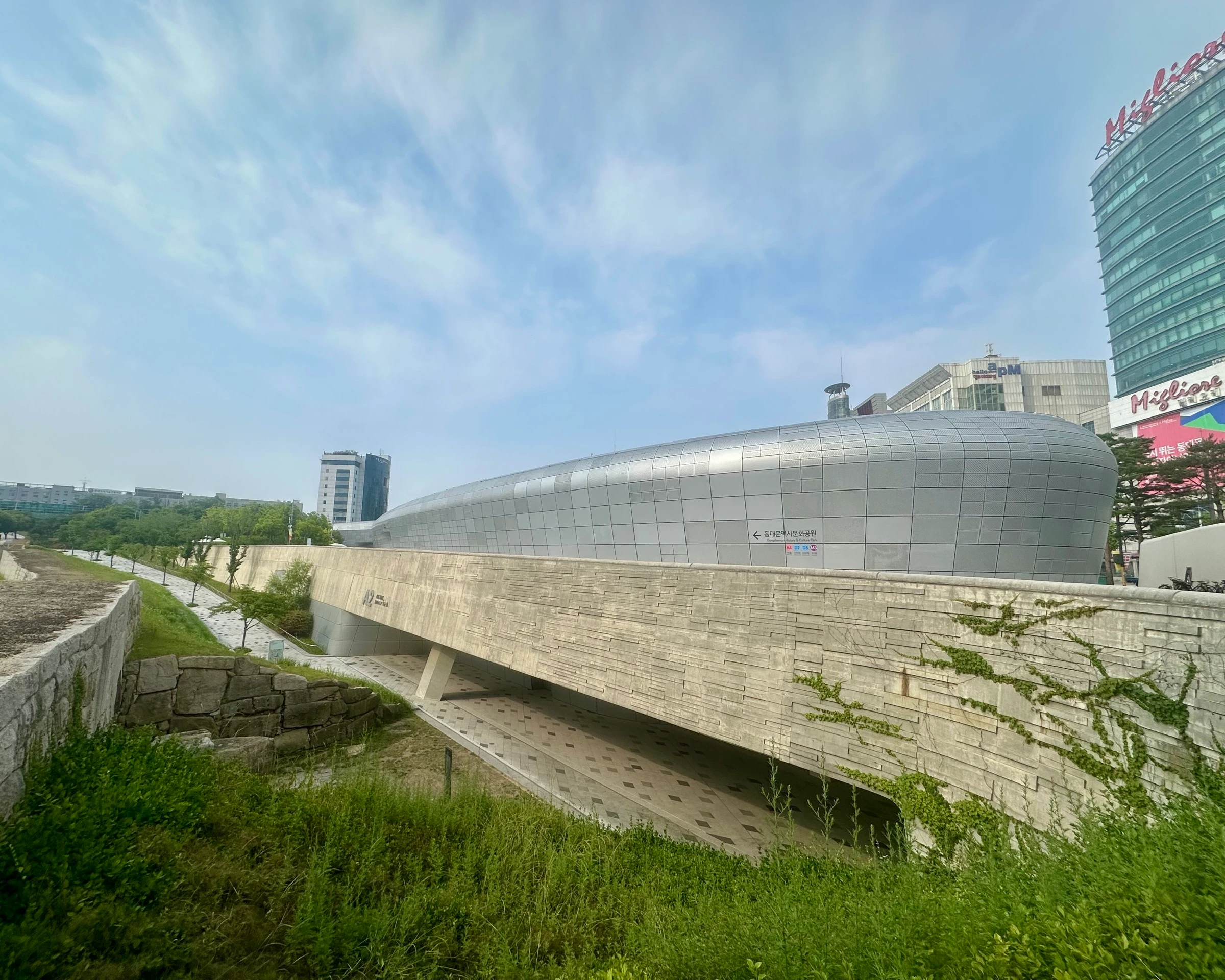 자하 하디드가 설계한 네오퓨처리즘 랜드마크, 동대문디자인플라자(DDP)의 흐르는 듯한 은빛 외관. 발굴해 보존한 옛 한양도성 구간 바로 옆으로 솟아 있습니다.