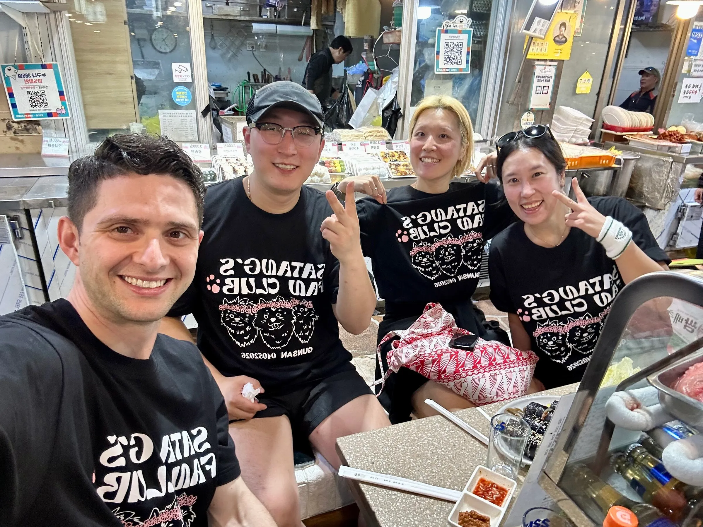 A small group in matching run-club shirts at a traditional Seoul market stall after a group run.