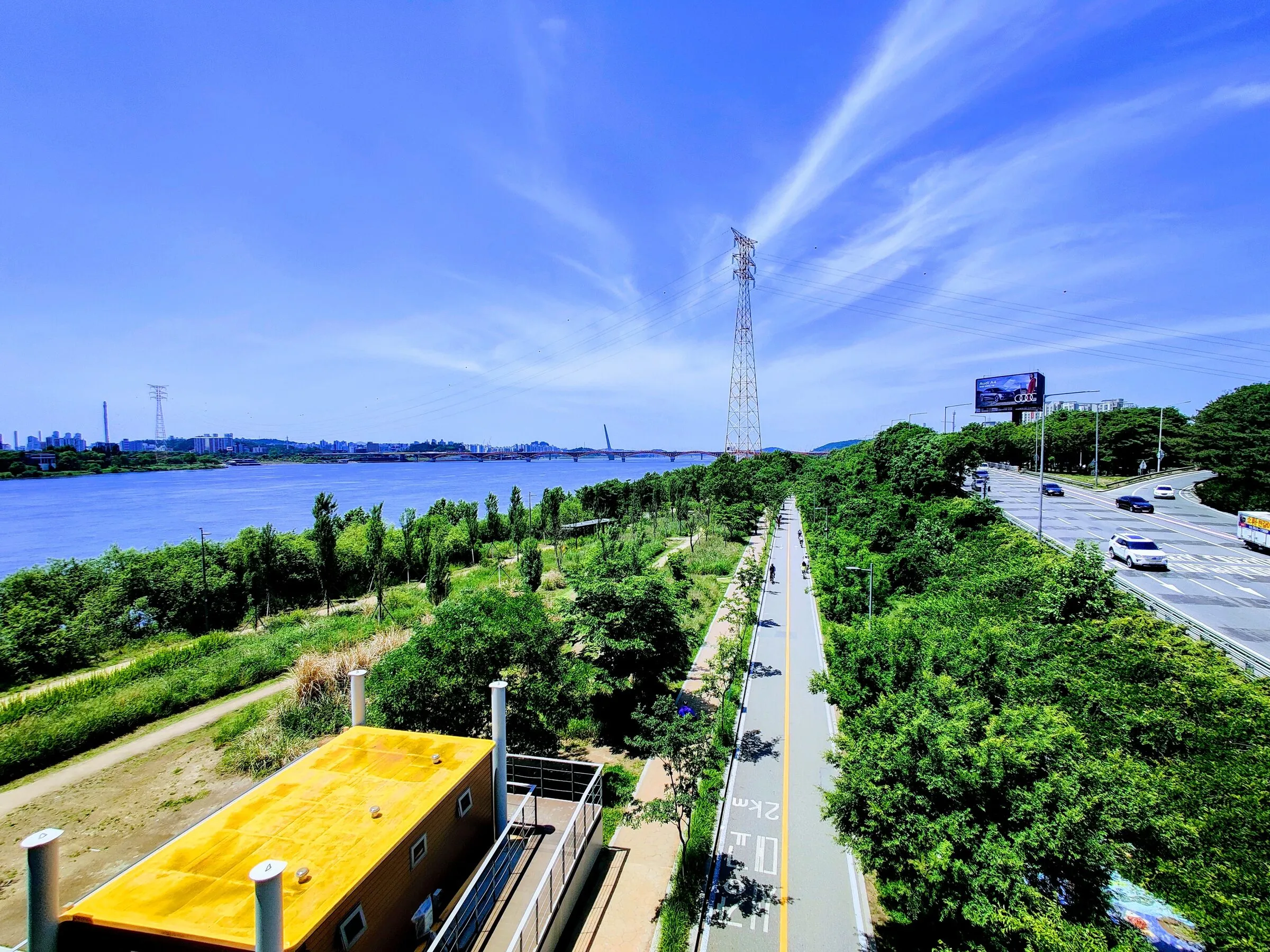 Wide green parkland and a curving bike path beside the Han River on a bright summer day.