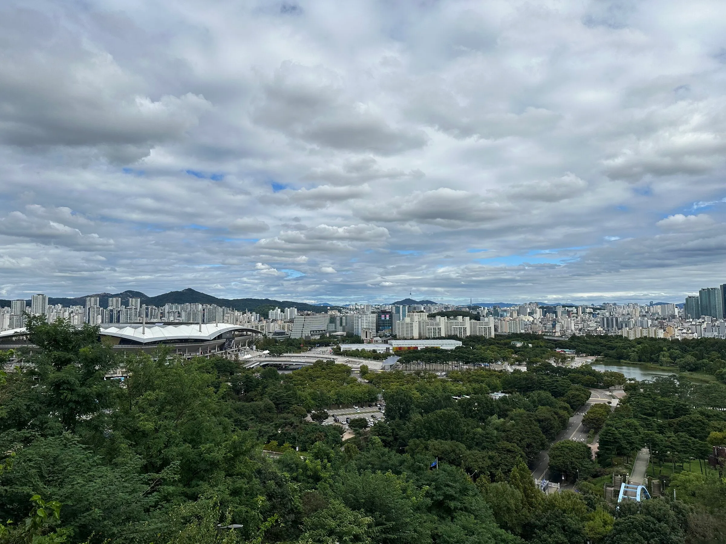 The Seoul skyline and northern mountains seen across the grass fields of Haneul Park in early autumn.