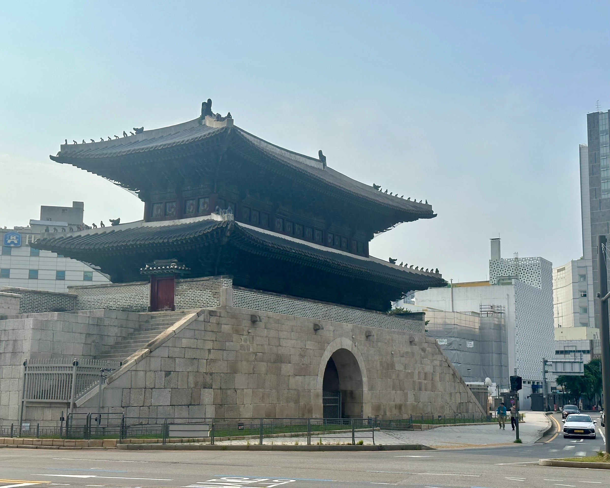 큰 동쪽 문 흥인지문(동대문). 석축 위에 2층 목조 문루가 올라앉고 아래로 홍예문이 뚫려 있으며, 흐린 하늘 아래 비둘기들이 처마를 따라 줄지어 앉아 있습니다.