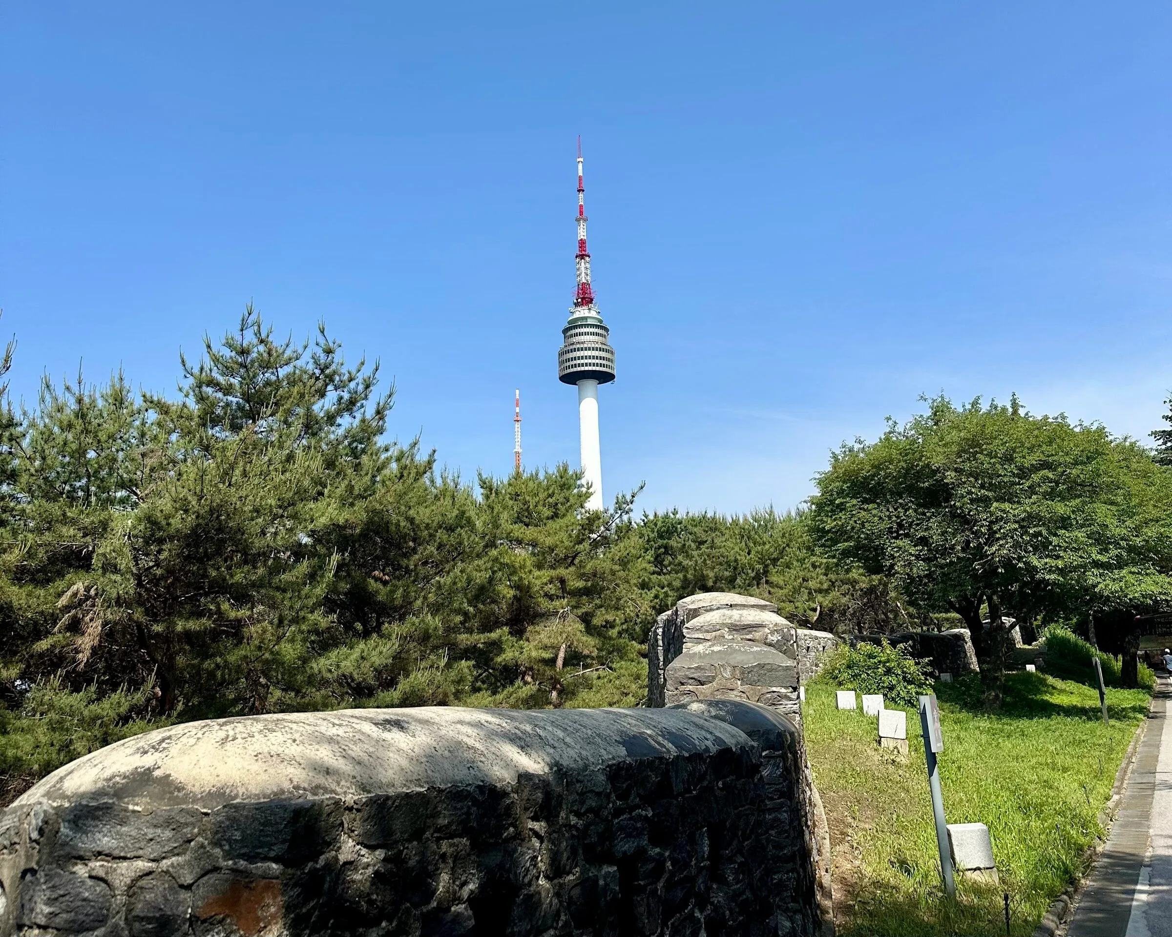 N Seoul Tower seen from the restored Namsan stretch of the Seoul city wall, white-and-red against summer sky.
