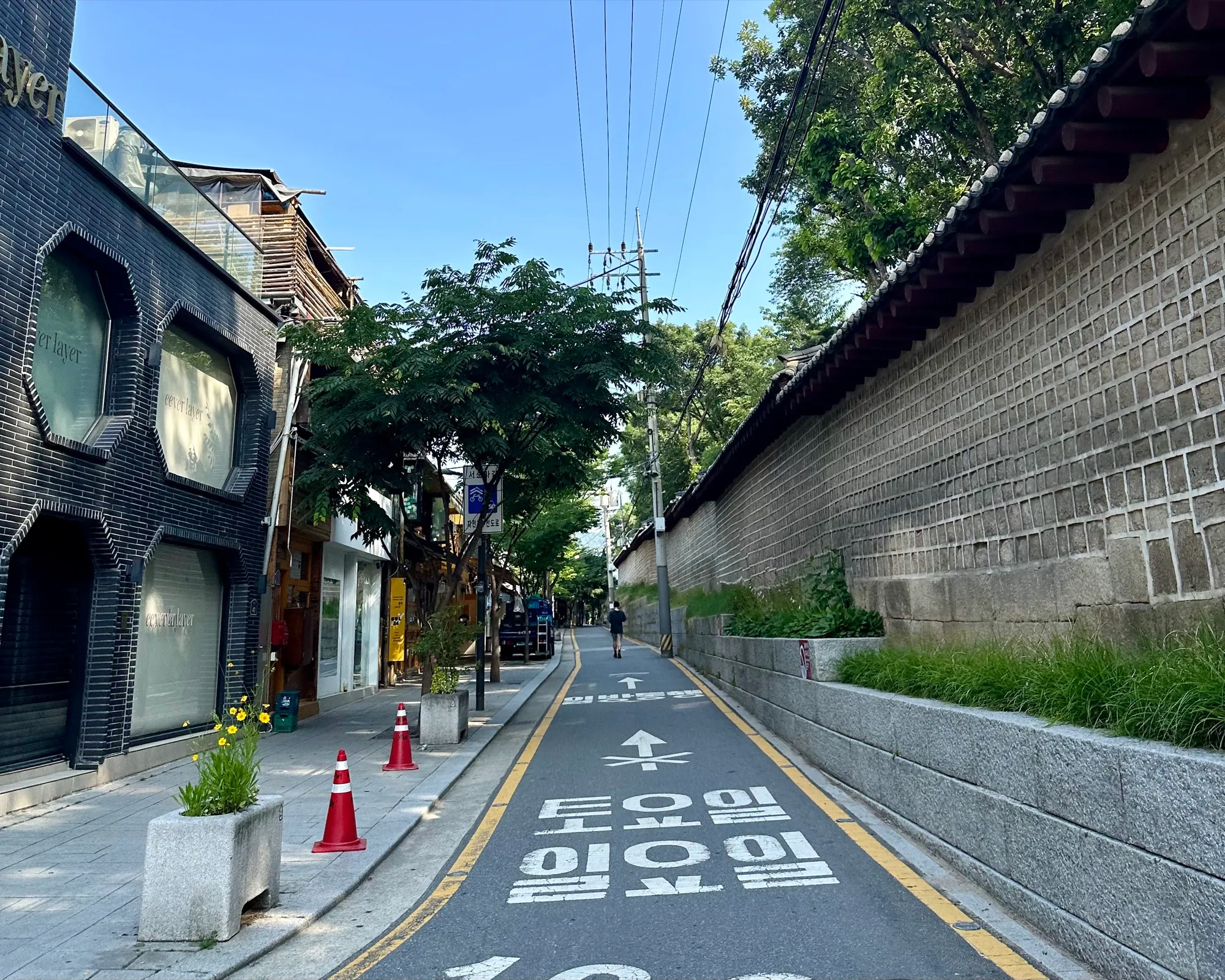 A quiet running lane alongside a traditional stone palace wall, cafes on the left and a lone runner ahead, bike-lane markings on the road.