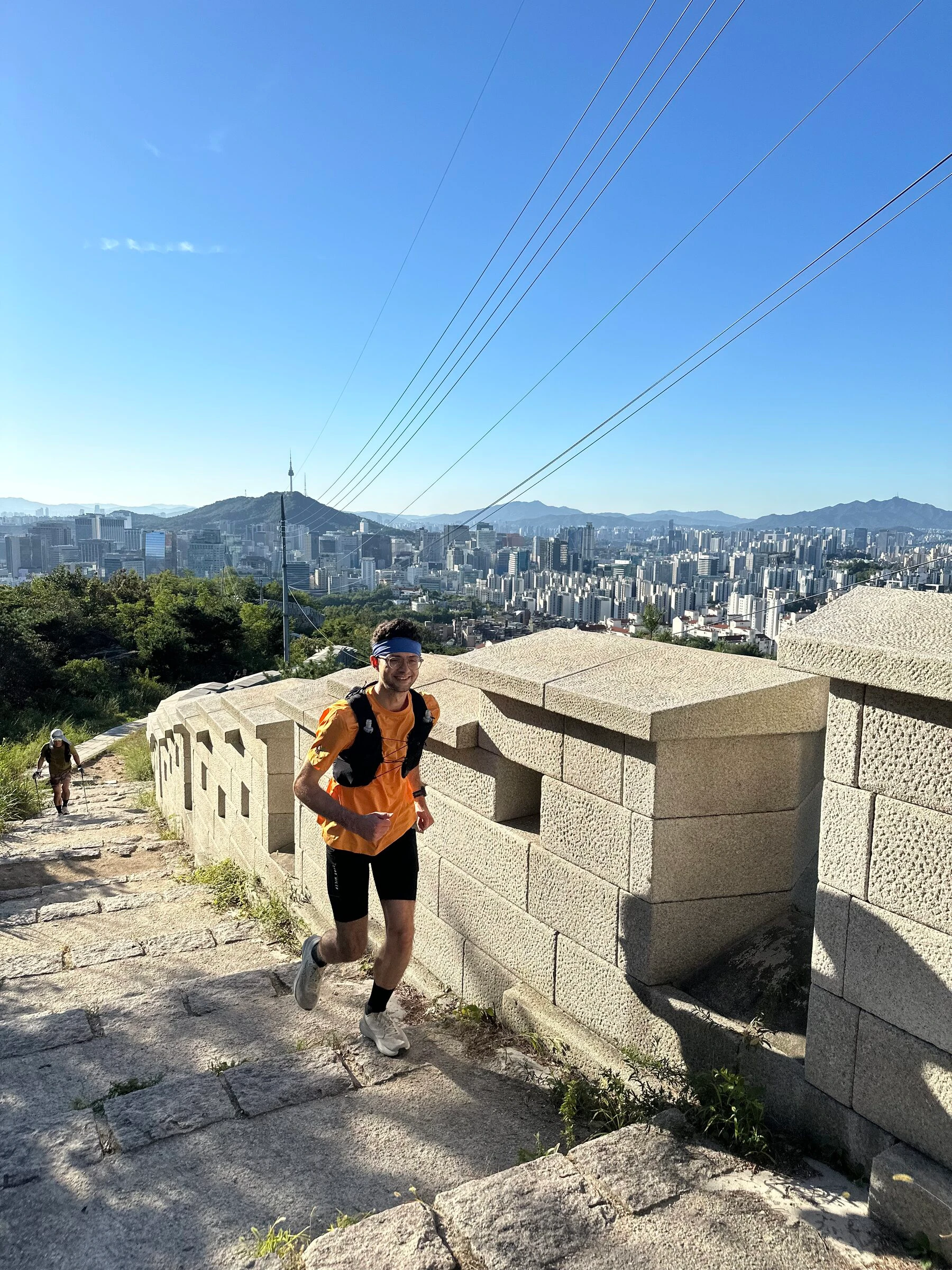 인왕산 높은 곳의 성곽길을 웃으며 달리는 퀸틴. 옆으로 화강암 성가퀴가 이어지고, 뒤로 서울 도심 전체가 펼쳐집니다.