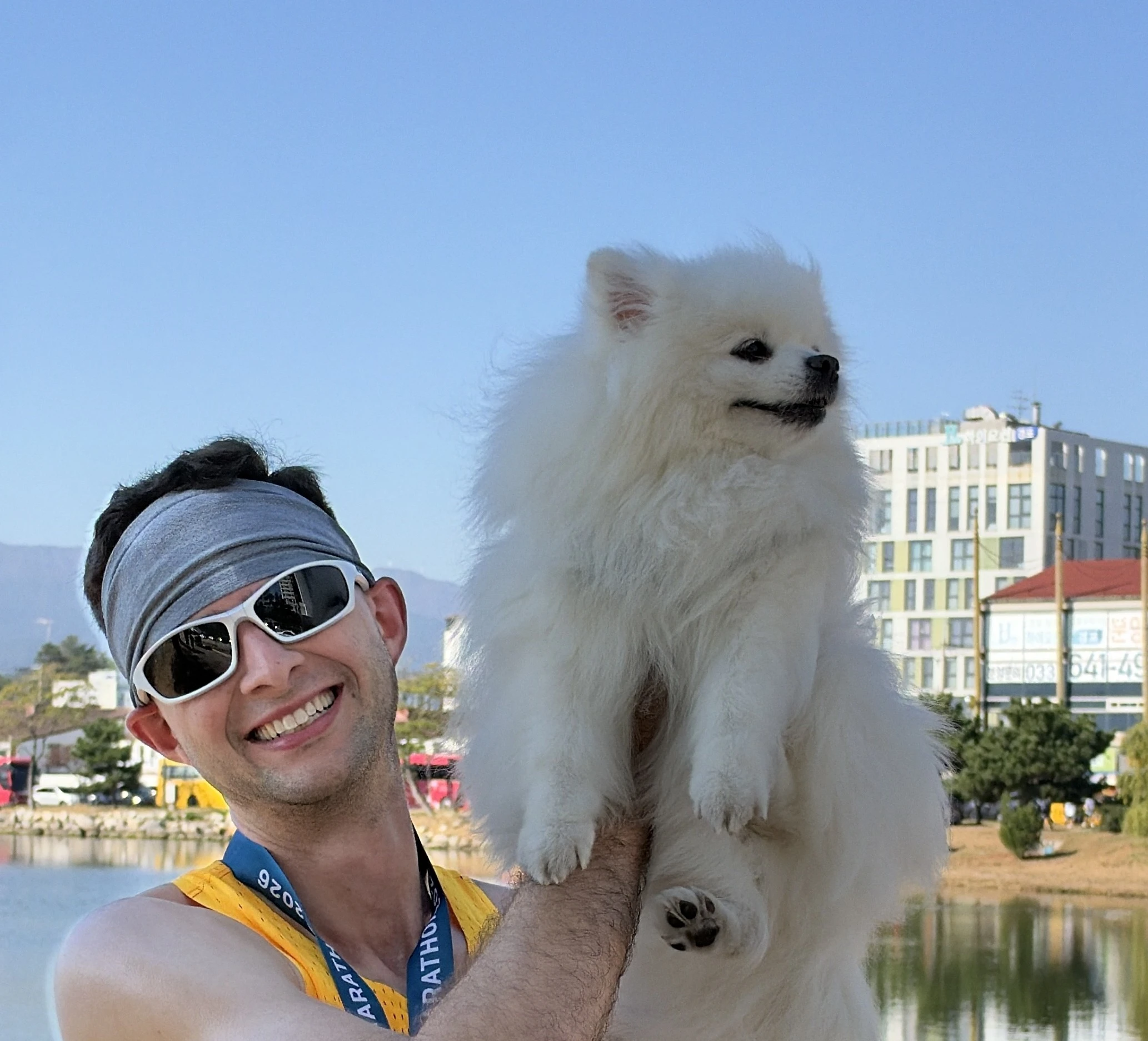 Quintin, wearing his finisher medal, holding up his Pomeranian, Satang, beside Gyeongpo Lake after the Gyeongpo Marathon half in Gangneung.