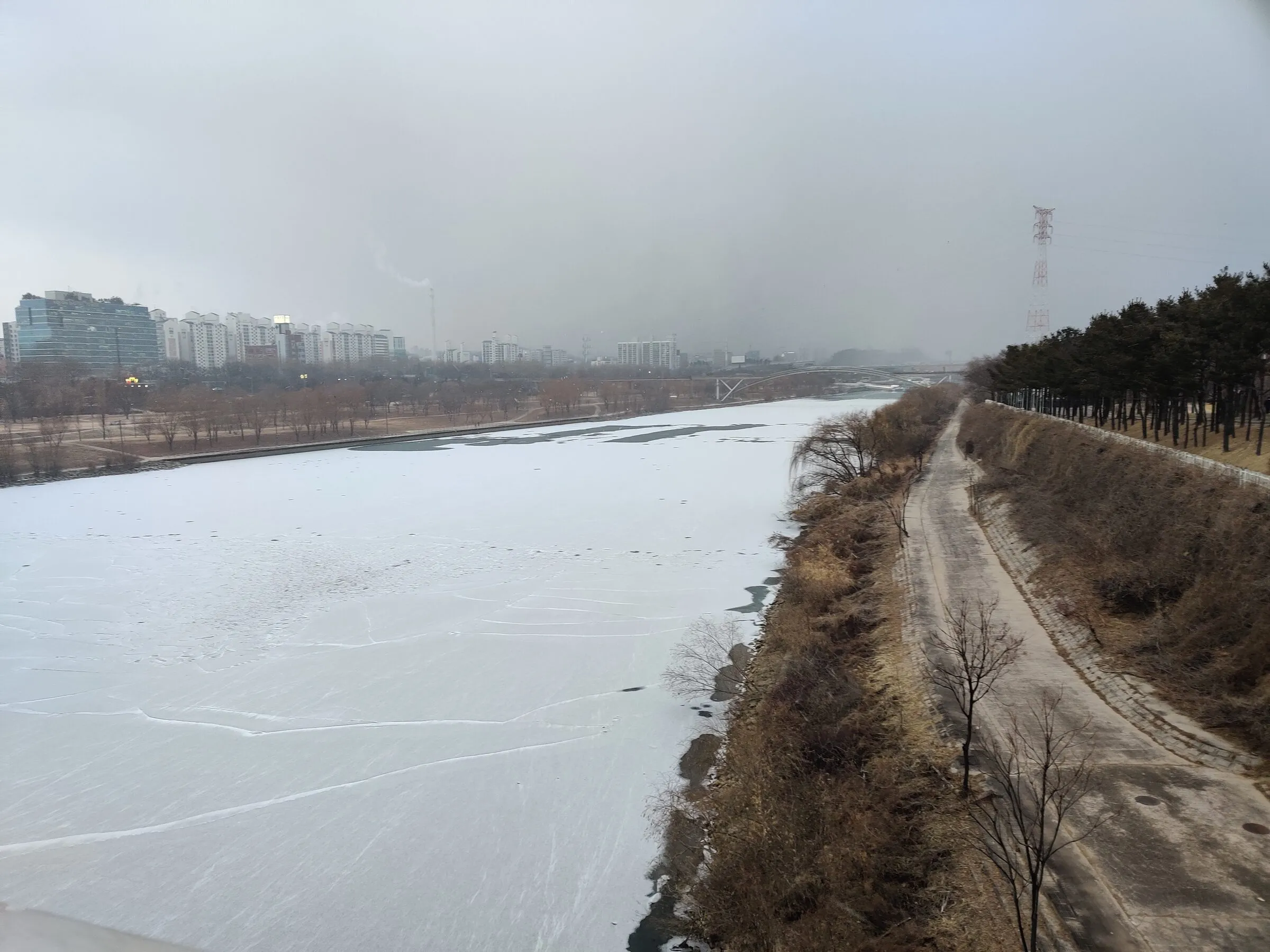 A snow-covered riverside trail tracing the frozen Han River.